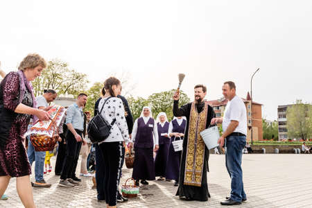 Beryoza, Belarus - April 27, 2019: The priest follows the Christian religious tradition of sprinkling believers and their Easter cakes, painted eggs and candles, with holy water, near the church.のeditorial素材