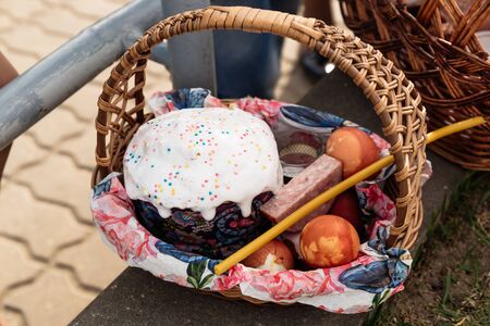 Easter straw basket decorated with a festive napkin with Easter cake and bright decorated eggs and a lit church candle. A festive treat and a peaceful mood.の写真素材