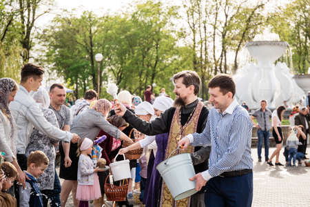 Beryoza, Belarus - April 27, 2019: The priest follows the Christian religious tradition of sprinkling believers and their Easter cakes, painted eggs and candles, with holy water, near the church.のeditorial素材