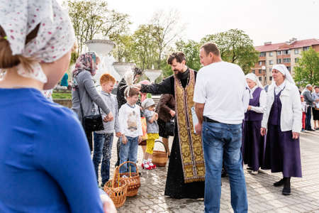 Beryoza, Belarus - April 27, 2019: The priest follows the Christian religious tradition of sprinkling believers and their Easter cakes, painted eggs and candles, with holy water, near the church.のeditorial素材