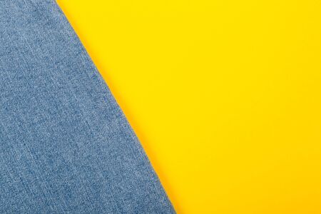Denim jeans with a bright texture lie diagonally on a yellow background. The modern trend of fashionable casual wear is suitable for people at any age. Close-up.の写真素材
