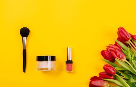 Tools for applying light refreshing makeup lie on a yellow background with a bouquet of red peonies. Bright spring-summer collection. Trendy background for advertising text. Top view.の写真素材