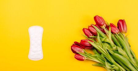 Top view of women's sanitary pads, panty liners on a yellow background. Flat lay with a bouquet of flowers.の写真素材