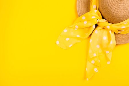 A straw hat with a polka dot scarf on a yellow background with an empty place for advertising and text. Top view.の写真素材