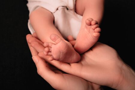 Little cute legs of a newborn baby lie on the palms of his mother. Caring for a natural or adopted child. Awakened maternal instinct and unconditional love. Close-up.の写真素材
