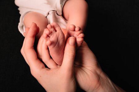 Little cute legs of a newborn baby lie on the palms of his mother. Caring for a natural or adopted...