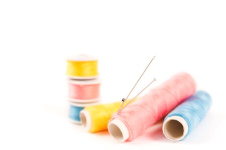 Three spools and bobbins of thread of yellow, blue and pink color with needles on a white background...