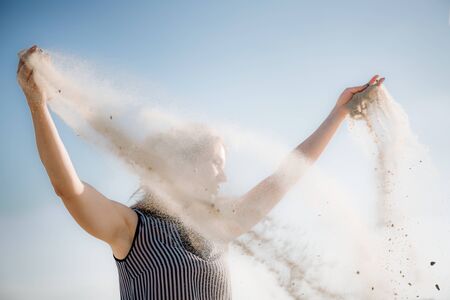 A young beautiful girl of European appearance with hidden skin scatters sand from her hands in the...