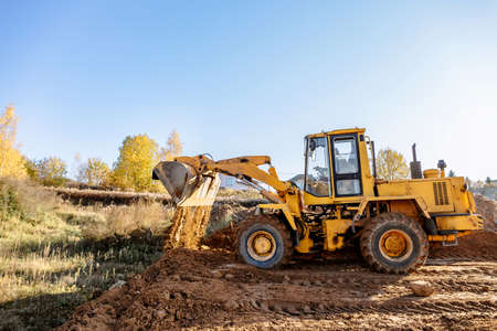 large yellow wheel loader aligns a piece of land for a new building. Preparation of the land for the auction. Leveling the landscape and adding sand for construction. Banner wallpaper.の写真素材