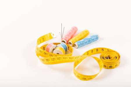 A centimeter tape and three spools of yellow, blue and pink thread on a white background in a minimalistic style with a place for text. Items for needlework, embroidery, sewing and cutting clothes. Studio shot, side view.の写真素材