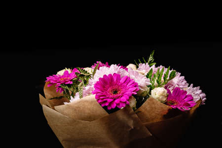 Large beautiful bouquet of chrysanthemums, gerberas, roses and ferns in pink and purple colors, packed in brown craft paper and isolated on a black background. Postcard for the holiday. Close-up.の写真素材