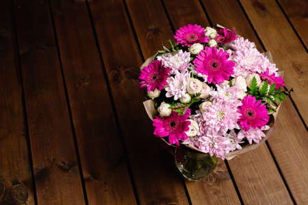 A large beautiful bouquet of chrysanthemums, gerberas, roses and ferns in pink and purple colors wrapped in brown craft paper on a wooden background. Postcard for the holiday. Close-up.の写真素材