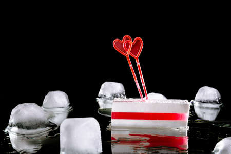 White sugar candy with layer of red marmalade and two heart shaped skewers. Melting ice cube on a...