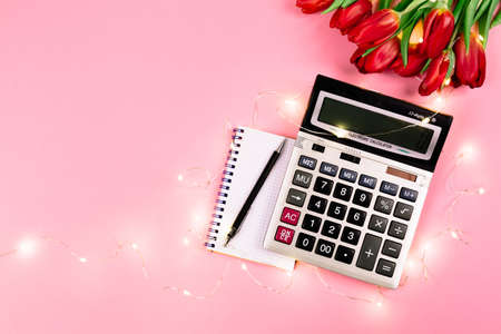 Large silver calculator, black pen, spiral notepad, lights garland and tulips bouquet lays on a pink background. Concept of business holiday and congratulating women on women's day at the workplace.の写真素材