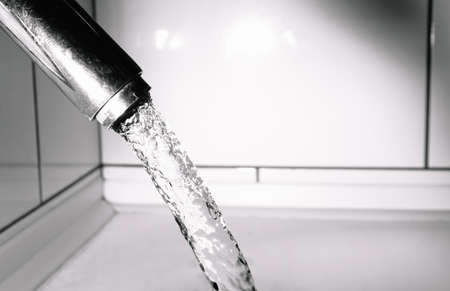 Pure and clear tap drinking water flows from the tap. Chrome plated fixtures are worn and have scratches and patches. Cleaning and hygiene in the bathroom. Close-up.の写真素材