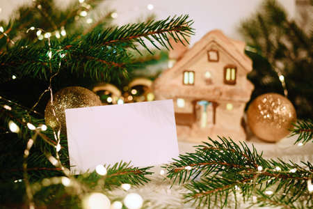 Blank business card with christmas tree branches, ceramic candlestick house and shiny balls. New year celebration concept banner. Gift certificate. Side view. Invitation to an event or corporate partyの写真素材