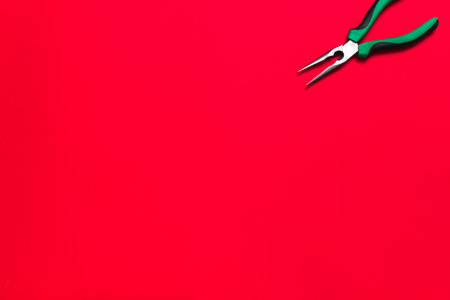Quality green building pliers tool to compress something or repair a car or house on red background. Do it yourself instrument. Banner for advertising construction shop with copy space. Business card.の写真素材