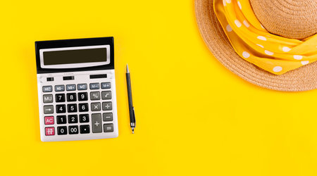 Big silver calculator, black pen and straw hat on a yellow background, with copy space. Conceptual photo of calculations tax holiday, vacation rest, travel budget. Summertime business card banner.の写真素材