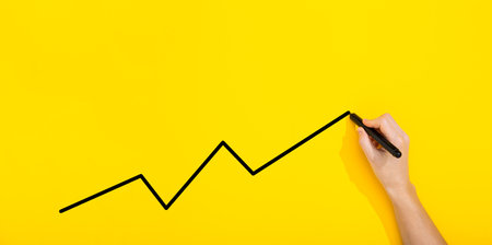 Black marker in female hand writes chart on yellow background with copy space, text place. School teaching. Sales. Advertisement banner. Business mockup. Writing board. Career growth. Success. Curve.の写真素材