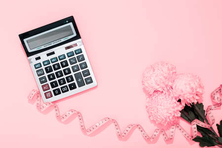 Big silver calculator and flower bouquet on a pink background with copy space. Concept of sewing business holiday and greeting card on woman day. Tax. Spring time. Calorie counting for weight loss.の写真素材