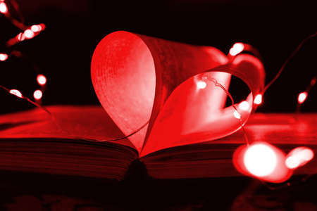 Red art book novel with sheets in the shape of a heart decorated with bright garland lights and highlights in the background, a romantic symbol of love, macro. Valentine day. Greeting card. Close up.の写真素材