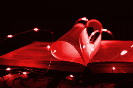 Red art book novel with sheets in the shape of a heart decorated with bright garland lights and...