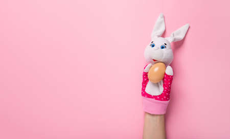 Banner with bunny and an Easter egg on pink background with copy space, empty text place. Christian holiday card. Springtime. Toy theater. Online course for painting eggs. Hand puppet. Childhood play.の写真素材