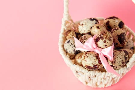 White basket with quail eggs, pink bow and pussy willow on paper background. Copy space. Easter...