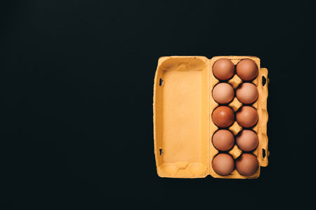 Natural organic chicken eggs in yellow cardboard package isolated on black background, top view, with copy space, empty text place. Business card of grocery store. Fresh farm food. Healthy eating. Tenの写真素材