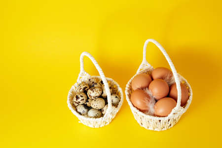 Two white handmade straw basket full of hen and quail eggs on yellow background. Copy space. Empty text place. Easter holiday card. Springtime mockup design. Healthy food product. Farm production.の写真素材