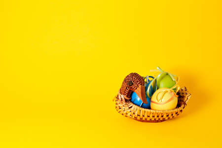 Handmade duck shaped straw basket with colorful painted eggs in satin bows and ribbons. Banner with yellow background. Copy space. Empty text place. Easter card. Interior decoration detail. Side view.の写真素材