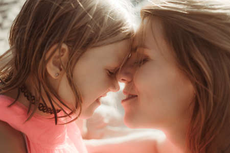 Sunny day, mom and daughter hug and chat together. Summertime vacation or holiday weekend on the beach. Psychology of communication of a single mother with a child. Close-up. Happy lifestyle moment.の写真素材