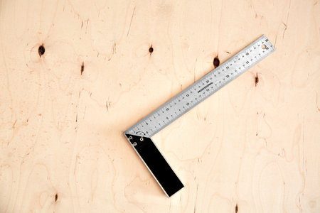 Steel framing set square on a wooden background. L-square instrument. Right angle. Silver color. Copy space. Plywood backdrop. Building rule. Measurement tool. Carpentry device. Triangle 90 degrees.の写真素材