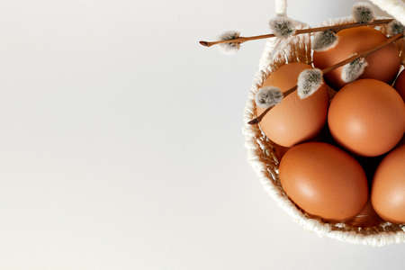 White background with handmade straw basket full of eggs, and pussy willow twig. Copy space. Empty place for text. Easter holiday card. Springtime mockup design. Healthy food product. Farm production.の写真素材
