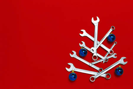 Christmas tree made of wrenches decorated with blue balls on red background.の写真素材