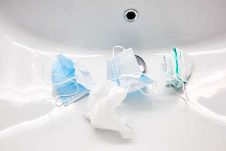 Used medical masks lie in the sink waiting a washing. White color bathroom. Disinfecting and saving money to be used again. Reusable. Family health care and save the budget concept. Epidemic hygiene.の写真素材