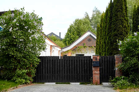 Black wooden fence with red brick posts. Entry group. Gates and wickets. Mailbox. Green spaces: thuja, lilac and other evergreens. Countryside private property. Landscaping design. Rural real estate.の写真素材