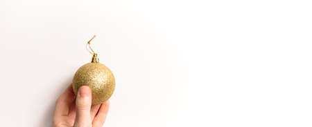Christmas tree toy in hand isolated on a white background. Copy space. New year glitter ball golden color. Holiday banner in fashion style. Close-up. Business card. Greeting certificate mockup design.の写真素材