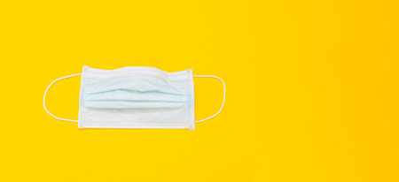 White medical disposable mask isolated on yellow background. Close-up. Banner. Copy space. Mockup design. Flat lay. Layout. Personal respiratory system protective equipment. Used material. Filtration.の写真素材