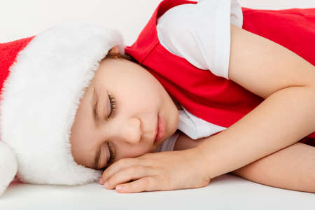 Portrait of beautiful sleeping child boy in red Santa Claus hat and costume isolated on a white background. Sweet dreams. Five-year little european kid. Close-up. Christmas mockup. New Year holiday.の写真素材