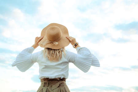 Straw hat with satin ribbon bow on young caucasian girl or woman. Back view close-up. Stylish accessory. Summer lifestyle. Freedom concept. Clothes element. Fashion. Natural background. Elegant style.の写真素材