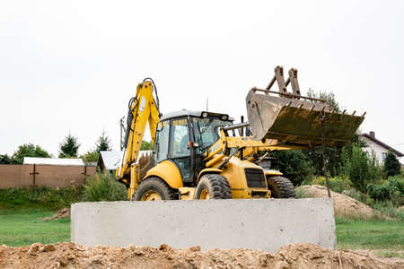 Wheel loader. Excavator install the foundation blocks into a trench. Retaining wall building. Construction site. Workers manage installing. Full HD footage video. Semkovo, Belarus - September 3, 2021.のeditorial素材