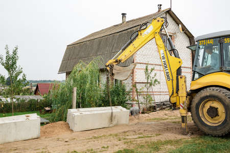 Wheel loader. Excavator install the foundation blocks into a trench. Retaining wall building. Construction site. Workers manage installing. Full HD footage video. Semkovo, Belarus - September 3, 2021.のeditorial素材