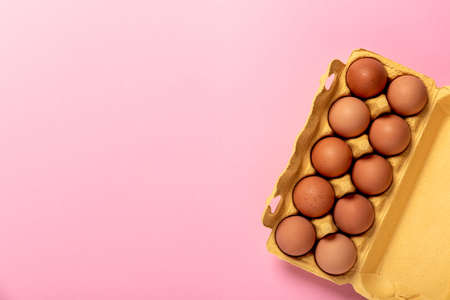 Natural organic chicken eggs in yellow cardboard package isolated on pink background, top view, with...