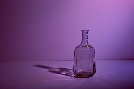 Glass empty open bottle with copy space. Graphic still life with light and shadow in lilac light. The concept of glass containers, recyclable materials or alcoholism. Large creative vase. Open flask.の写真素材