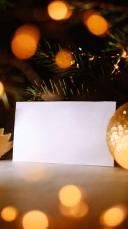 Blank business card with christmas tree branches and golden garland lights. New year celebration concept. Gift certificate. Side view. Cozy frame decoration. Invitation to an event or party.の写真素材