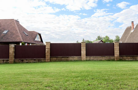Brown metal profile fence with block posts. Incline construction. Corrugated surface. security....