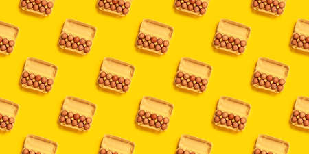 Seamless pattern. Natural organic chicken eggs in cardboard package isolated on yellow background, top view, copy space. Food banner. Business card of grocery store. Fresh eco farm product. Textureの写真素材
