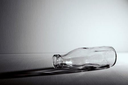 An empty glass bottle lies on the table. copyspace. Graphic still life with light and shadow in black and white colors. Concept of recyclable materials or alcoholism problems. depressive condition.の写真素材