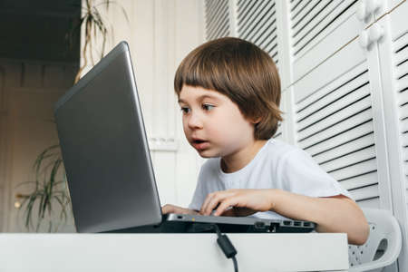 5 year boy sit at the table, uses laptop, looking very close and long time at the screen. Child is...